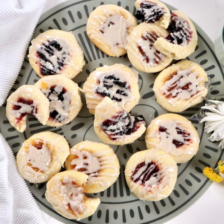 Fresh baked kolaches with golden edges, jam-filled centers, and a sweet powdered sugar icing drizzle