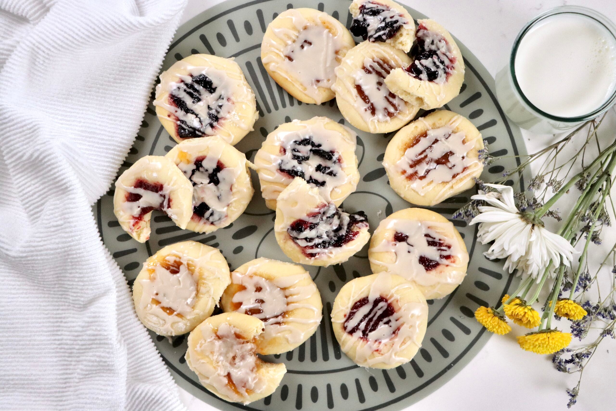 Fresh baked kolaches with golden edges, jam-filled centers, and a sweet powdered sugar icing drizzle