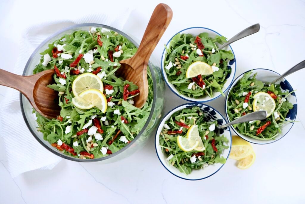A fresh lemon arugula salad with goat cheese, pine nuts, and sundried tomatoes served in a bowl.