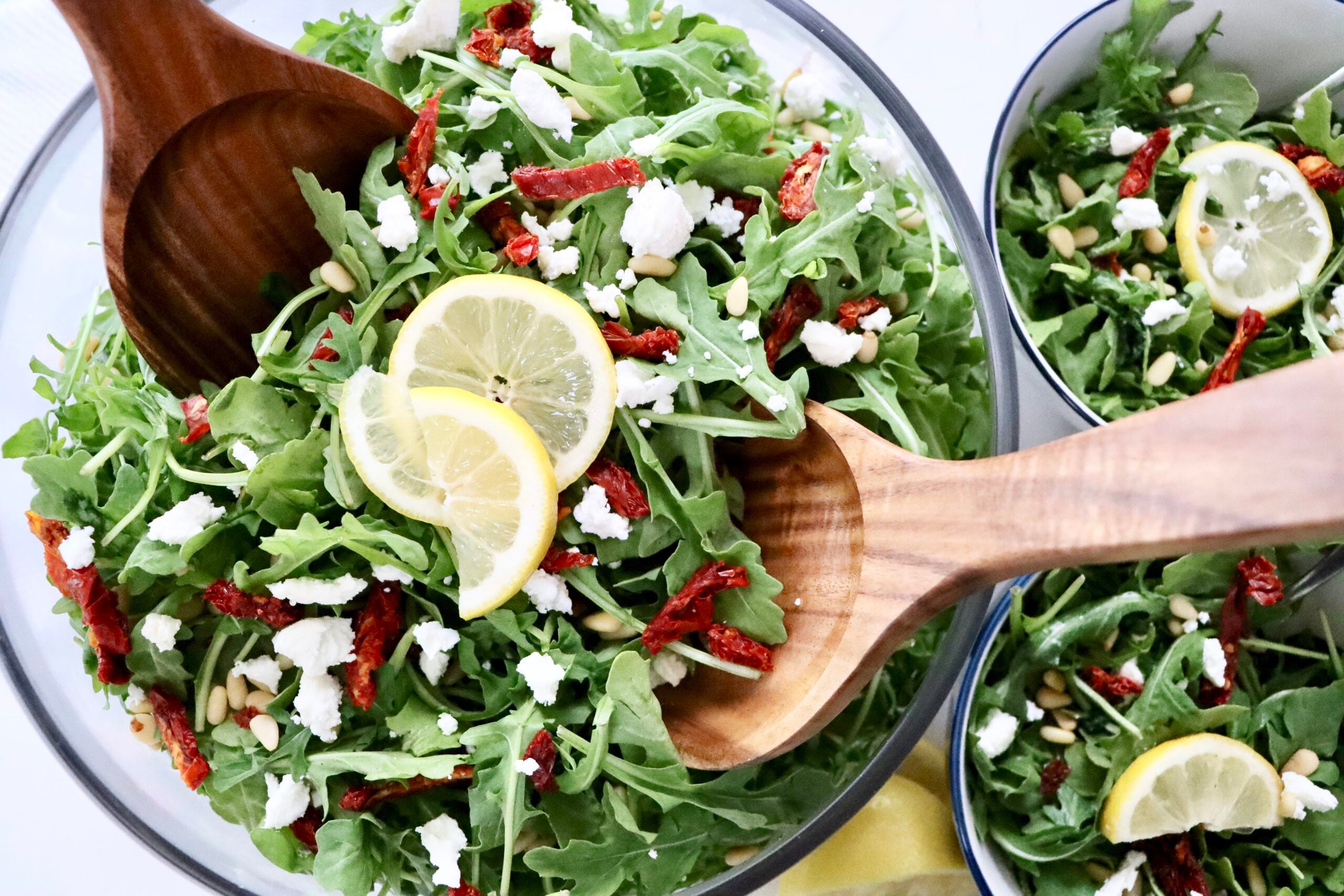 Close up of a healthy arugula salad with lemon dressing, goat cheese, pine nuts, and sundried tomatoes.