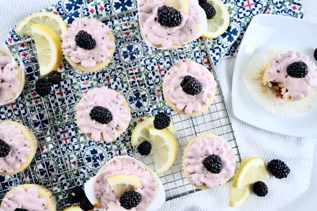 Freshly baked lemon blackberry cupcakes cooling on a rack with homemade berry frosting.