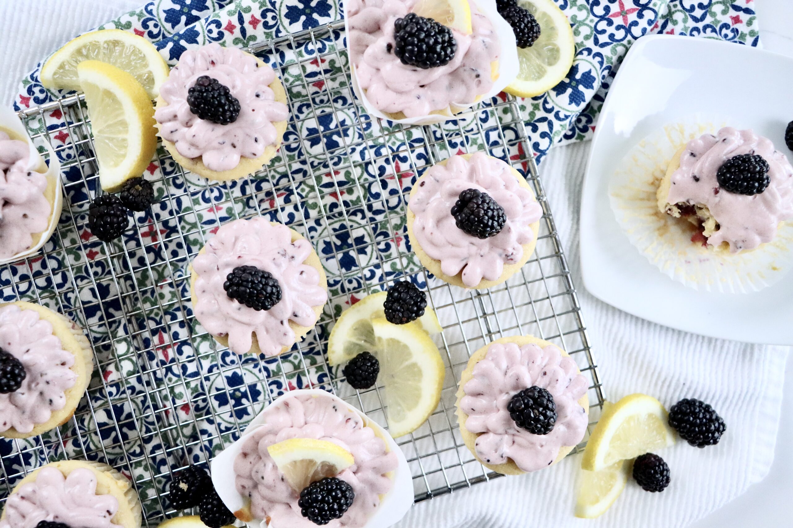 Freshly baked lemon blackberry cupcakes cooling on a rack with homemade berry frosting.