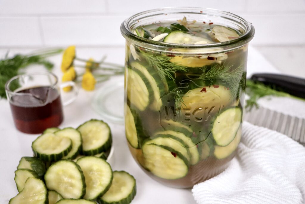 Homemade refrigerator sweet pickles packed in a mason jar with visible cucumbers, garlic, and herbs.