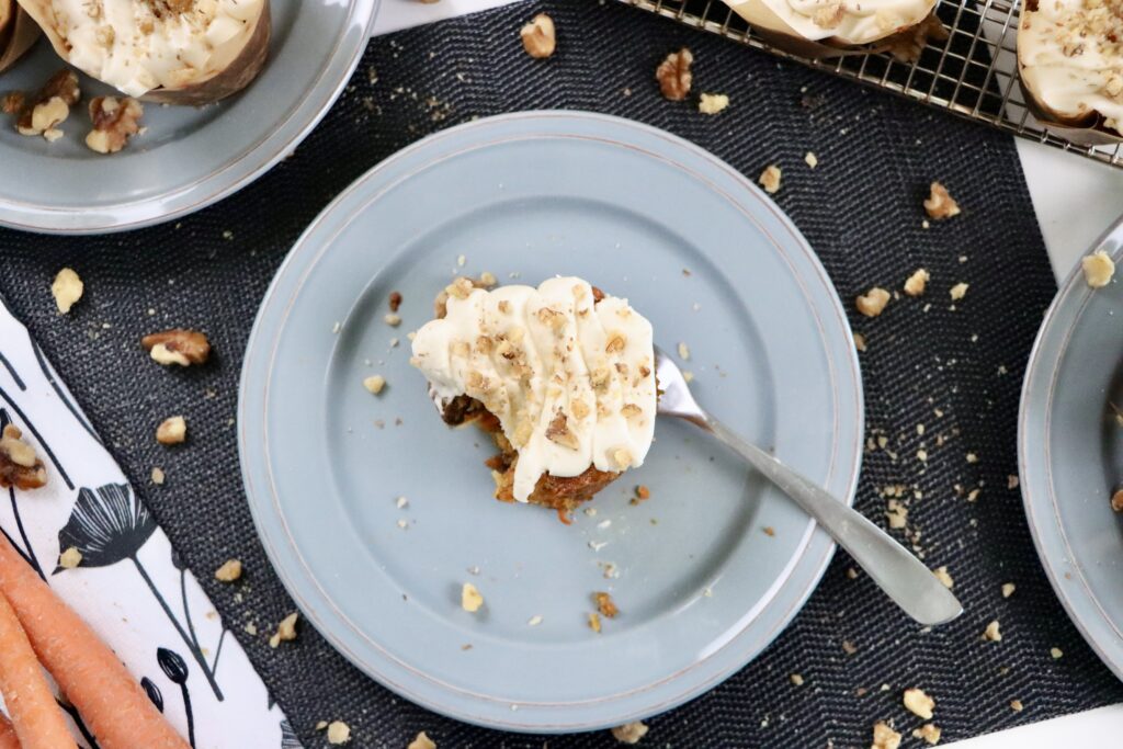 Moist carrot cake cupcakes topped with cream cheese buttercream frosting and crushed walnuts on a white plate