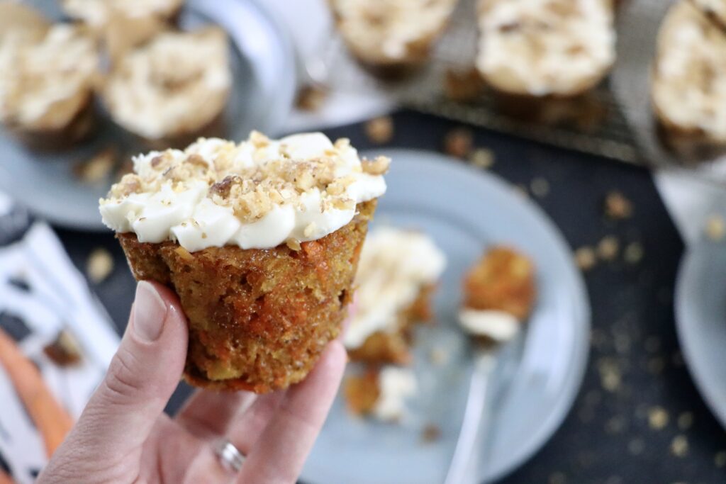Close up of soft carrot cake cupcakes with creamy frosting and chopped walnuts on top