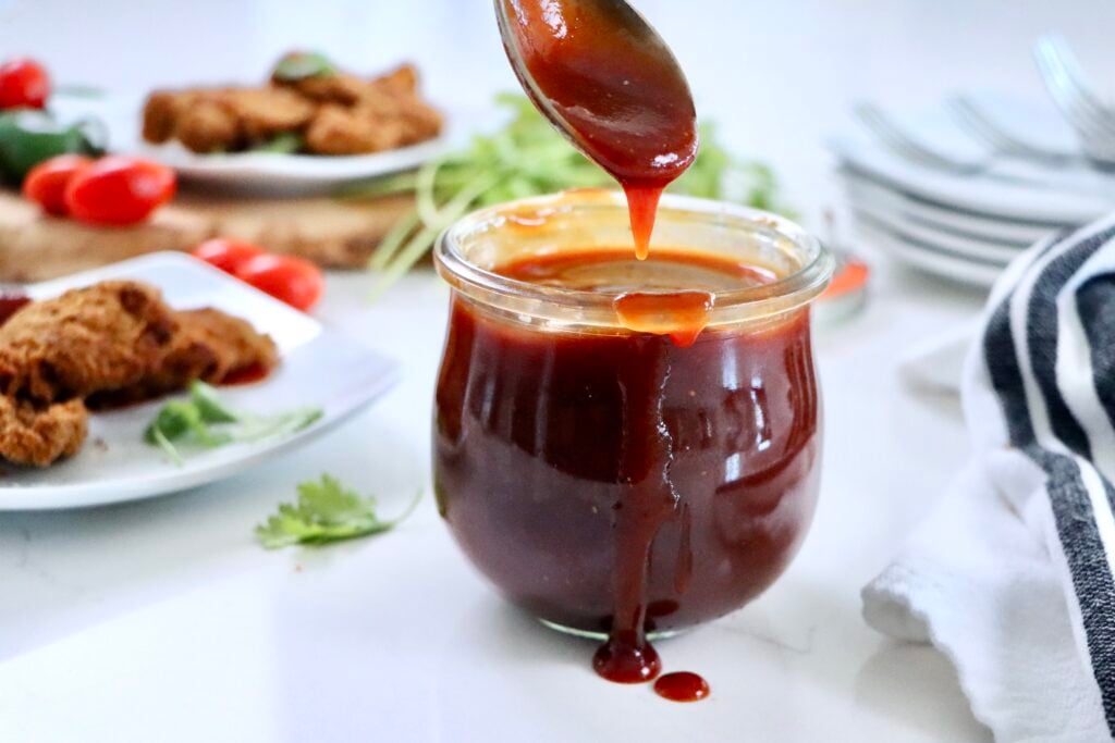 Freshly made BBQ sauce in a glass jar on a kitchen counter, made from ketchup, honey, vinegar, and spices.
