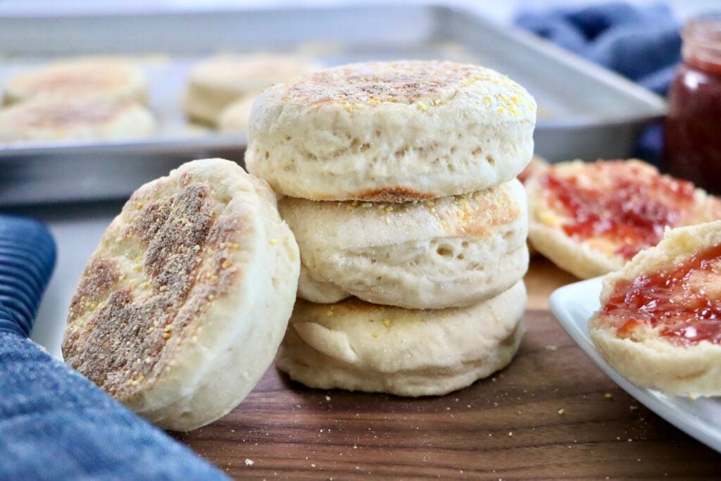 Soft and fluffy quick sourdough discard English muffins stacked on a cutting board with a golden brown crust and visible cornmeal coating.