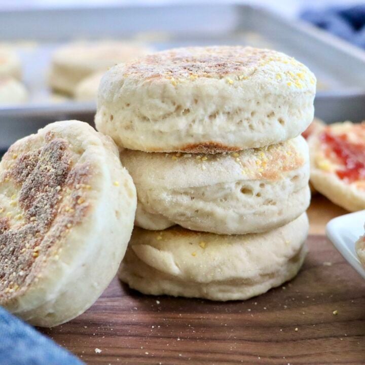 Soft and fluffy quick sourdough discard English muffins stacked on a cutting board with a golden brown crust and visible cornmeal coating.