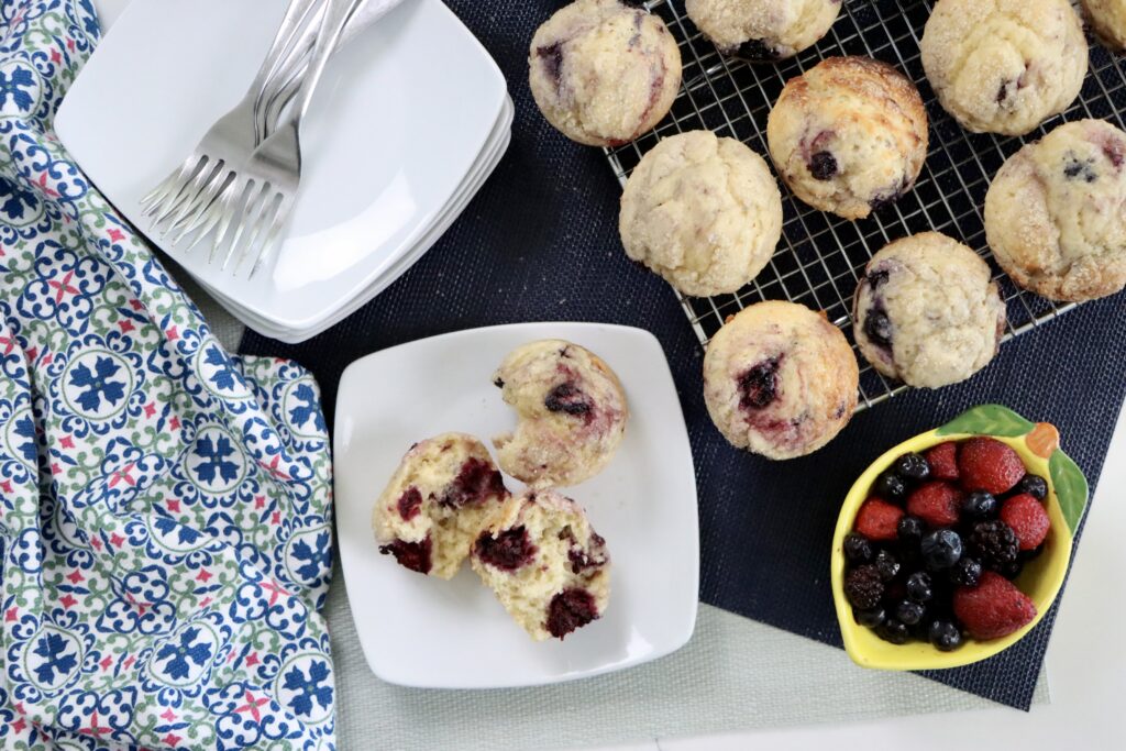 Freshly baked sourdough mixed berry muffins cooling on a wire rack with golden tops and juicy berries.