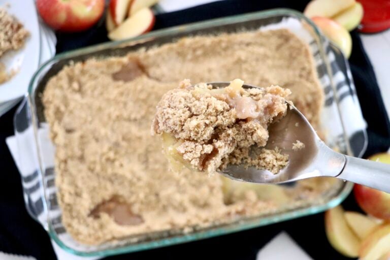 Spoon lifting a serving of warm apple crisp from the pan, steam rising