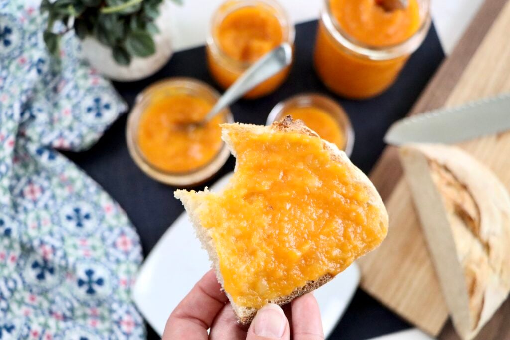 Close-up of glossy apricot pineapple jam being spread on a sourdough bread