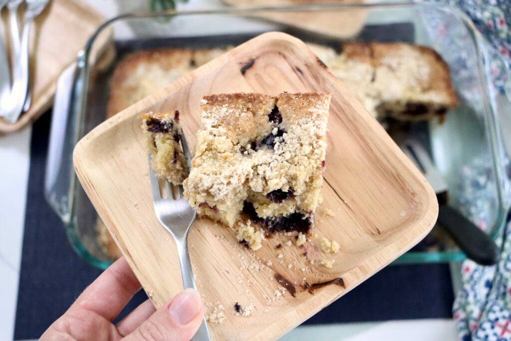 Slice of berry crumb cake on a plate showing soft crumb and juicy mixed berries