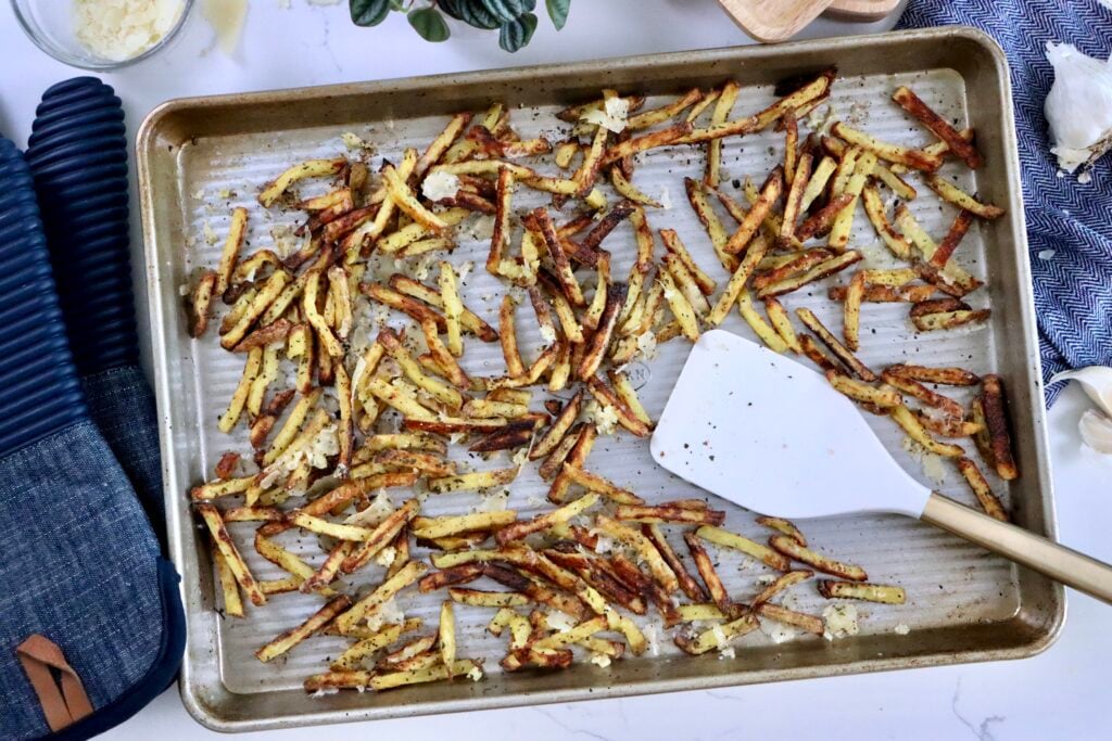 Crispy garlic parmesan fries topped with melted cheese and fresh garlic on a baking sheet