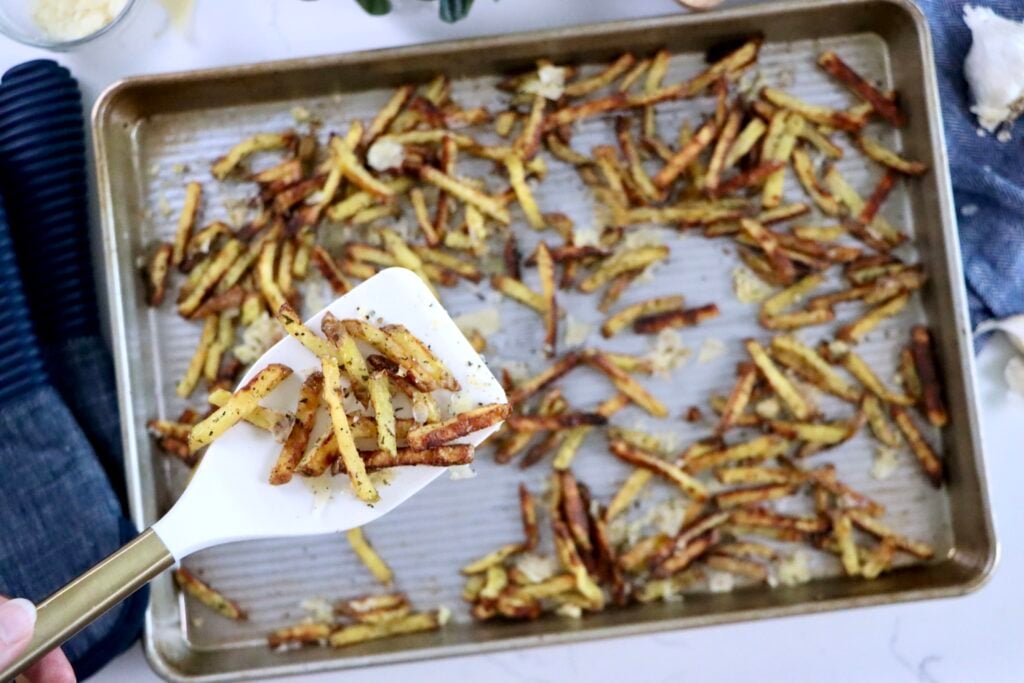 Hand tossing hot fries with shredded parmesan and diced garlic on a sheet pan