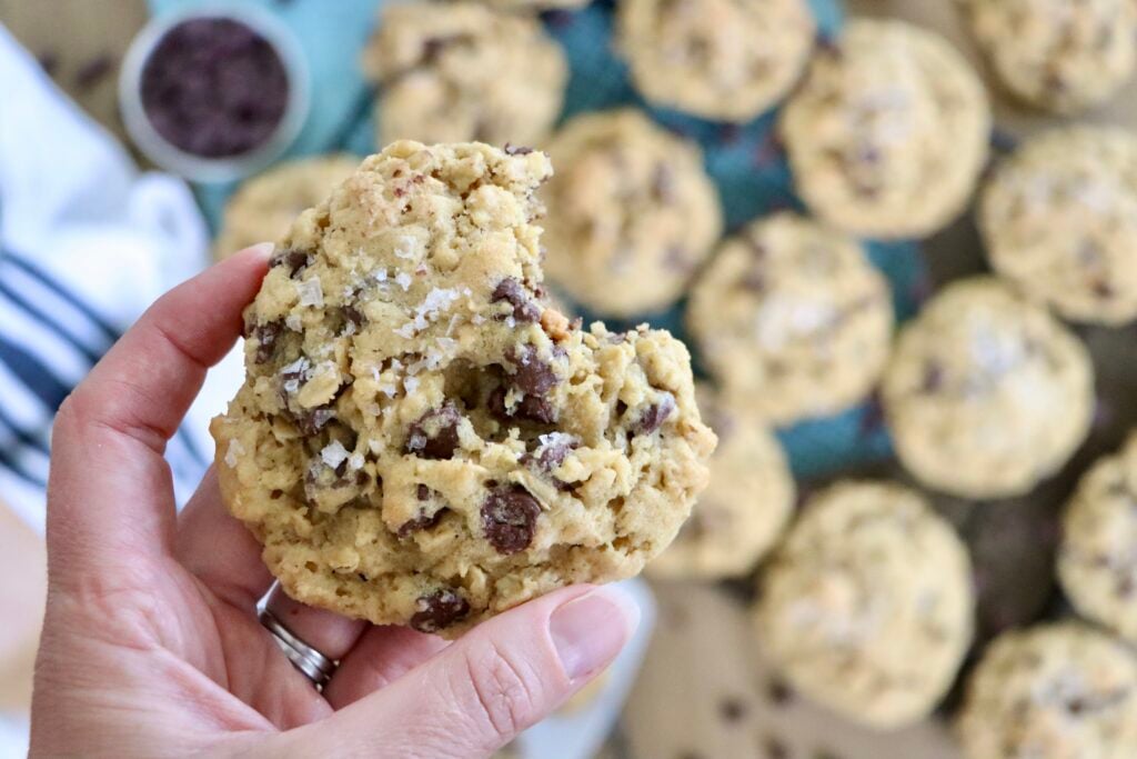 Hand holding a warm oatmeal chocolate chip cookie with a bite taken out