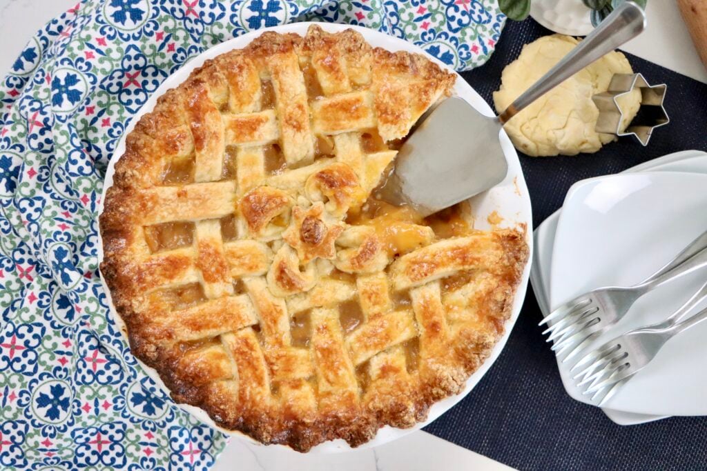Golden lattice-top peach pie fresh out of the oven with filling bubbling through the crust