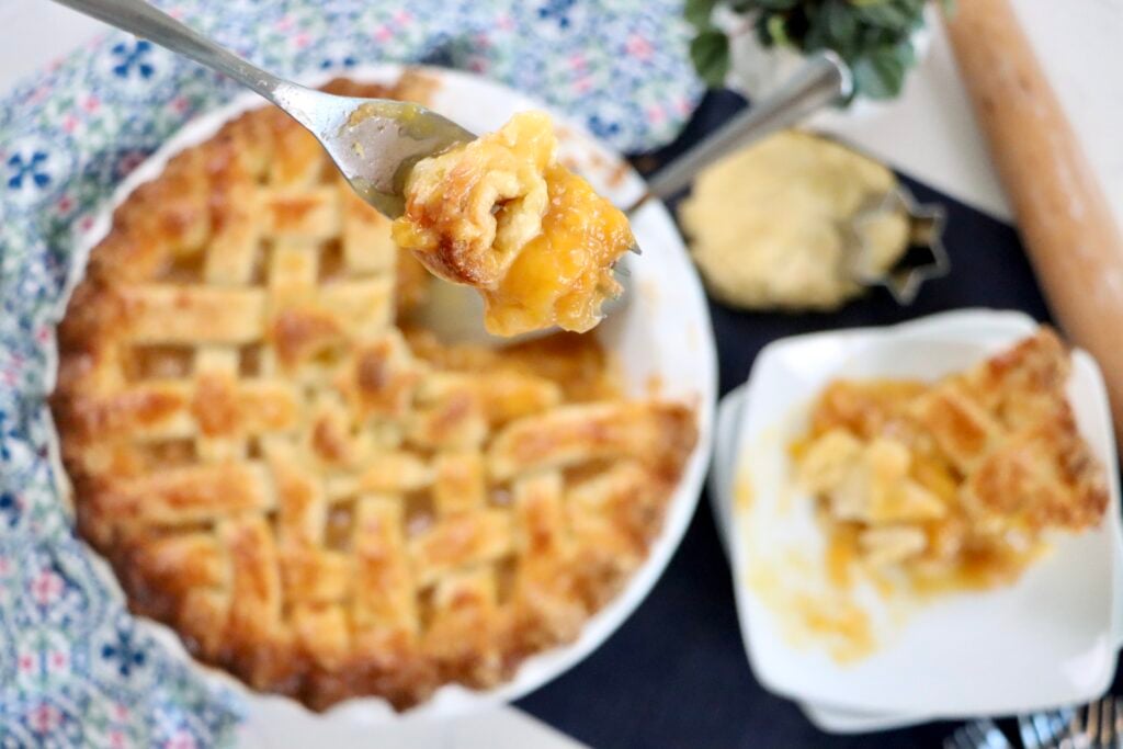 Fork cutting into a slice of homemade peach pie with a flaky crust