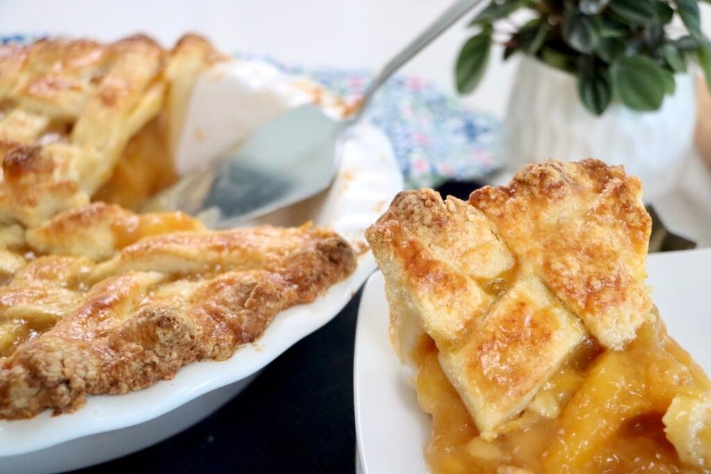 Slice of peach pie on a white plate showing thick, set peach filling