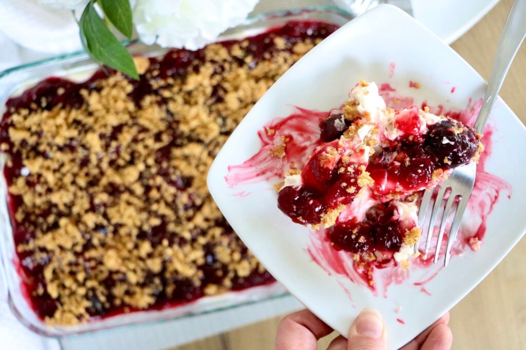 cherry yum yum dessert on a white plate with visible graham cracker, cream, and cherry layers