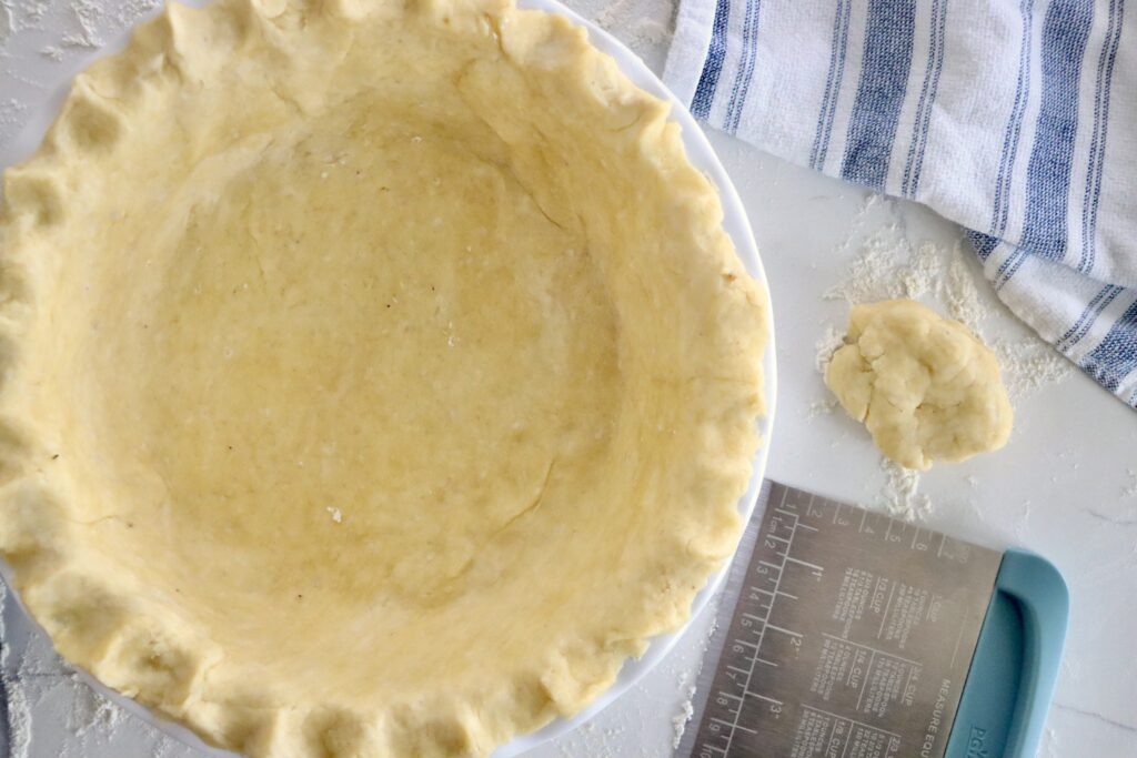 Unbaked pie crust crimped by hand around the edge of a pie plate