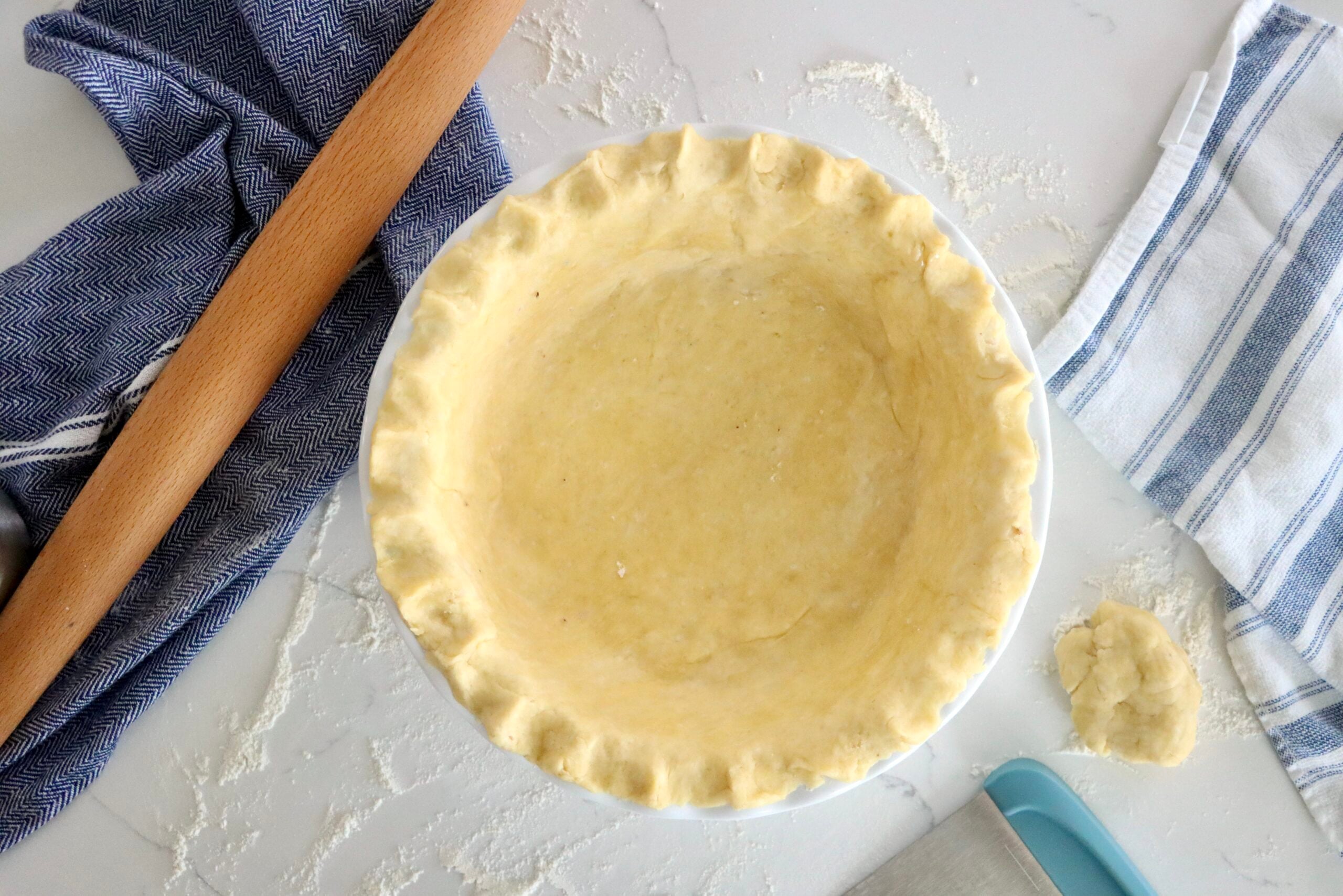 Unbaked pie crust crimped by hand around the edge of a pie plate