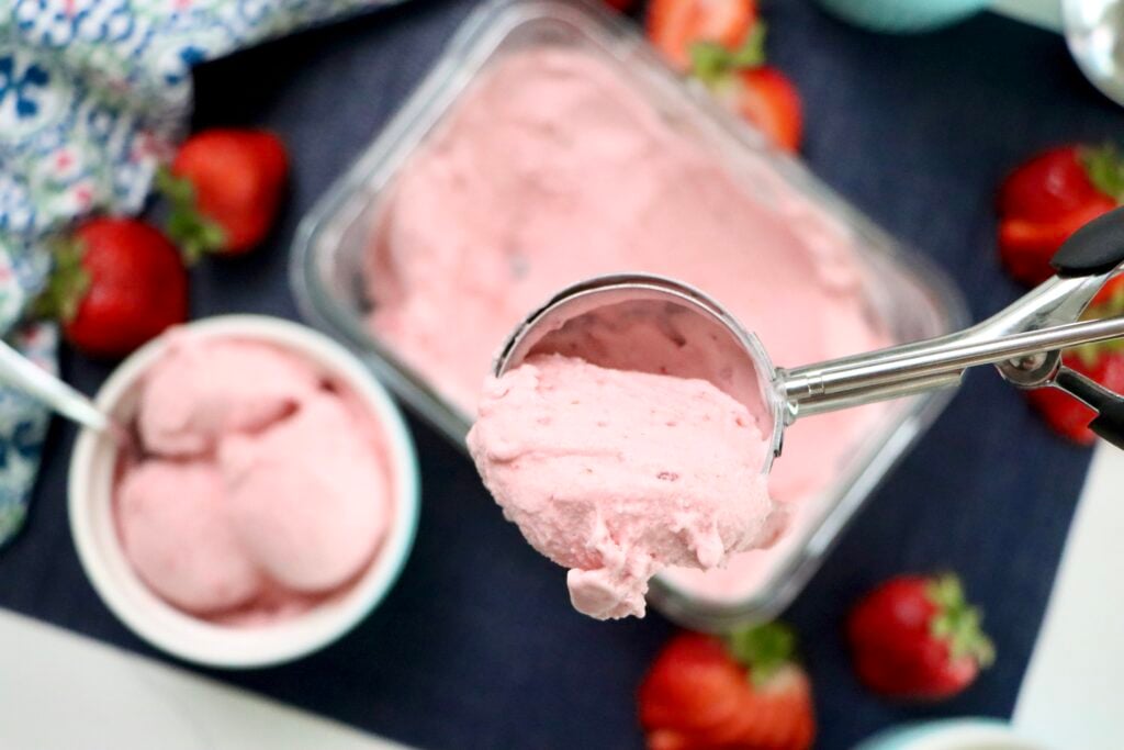 Scoop of strawberry ice cream being lifted from a container