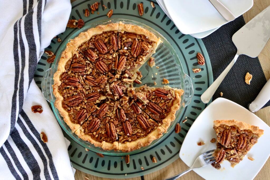 Overhead view of whole maple pecan pie topped with pecans with a slice on a white plate