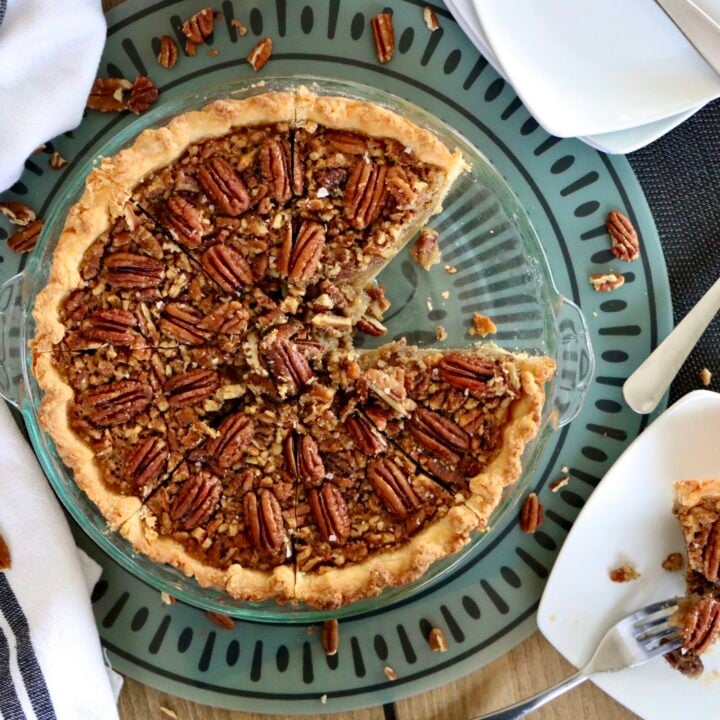 Overhead view of whole maple pecan pie topped with pecans with a slice on a white plate